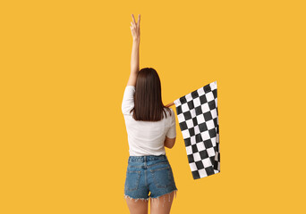 Young woman with racing flag showing victory gesture on yellow background