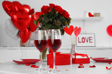 Fototapeta na wymiar Festive table serving with glasses of wine, roses, petals and gift boxes. Valentine's Day celebration