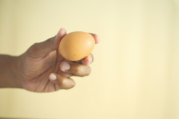 close up of men hand holding a egg against orange color background 