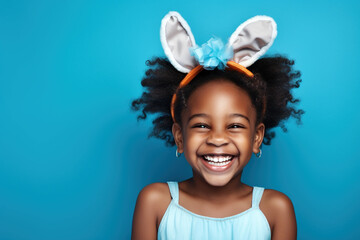 Portrait of an African cheerfully laughing girl with bunny ears on a blue background. Holiday traditions concept.