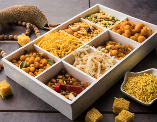 indian tea time snacks like sev, chivda, farsan, mixture, boondi, bakarwadi etc served in white wooden box with cells