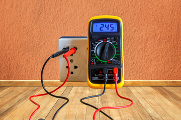 A digital multimeter is measuring the voltage of the electric plug on concrete wall in home.