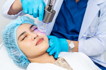 Asian Doctor doing laser on the woman face at beauty clinic. Beautiful woman having facial skin...