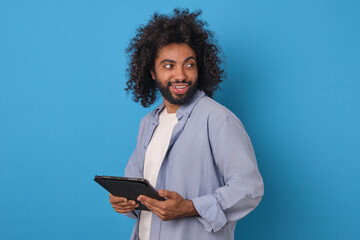 Young curly positive Arabian man freelancer with tablet computer in hands looks back rejoicing at...