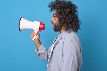 Young screaming ethnic Arabian man marketer with megaphone in hands stands sideways to camera and...