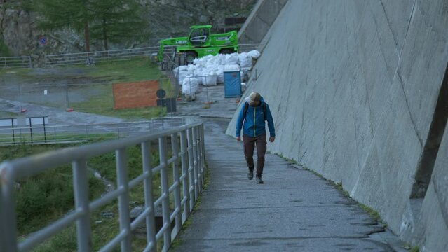 man walking along a concrete path and a metal railing.