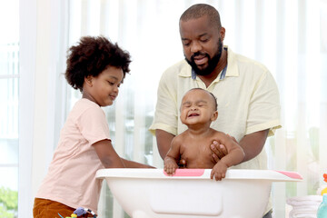 Happy African family, father bathing kid in tub, dad and son brother washing and cleaning little...