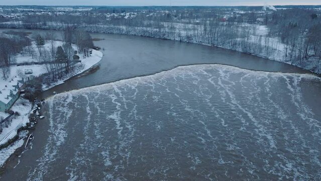 Aerial establishing view of Venta river rapids (Ventas rumba) during winter flood, old red brick bridge, Kuldiga, Latvia, overcast winter day, wide drone shot moving backward
