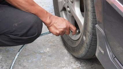 Klaten, Indonesia - August 17 2023: man driver hand inflating tires of vehicle, removing tire valve nitrogen cap for checking air pressure and filling air on car wheel at gas station.