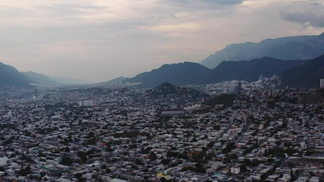 Wide aerial view of Monterrey, Mexico and buildings packed into the valley between steep mountains. Urban Mexico, Nuevo Leon, establishing shot. Drone pan left.