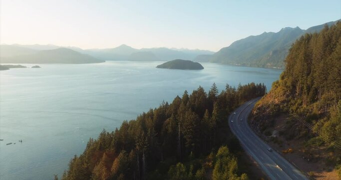 Aerial view of trans-Canada Highway along Horseshoe Bay, West Vancouver, British Columbia. Stunning drone footage of forest and sea with soft golden light. Forward flight.