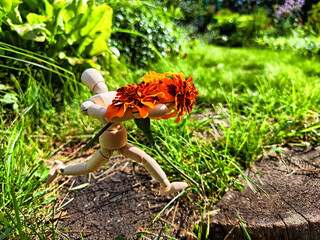 Wooden toy man with flowers against background grass in nature. Concept of holiday, gift bouquet, Valentine's Day, proposal, engagement, declaration of love, Mother's Day. Caring, loving, romantic