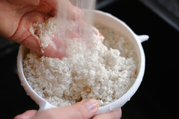 woman rinses rice under running water close-up of hands