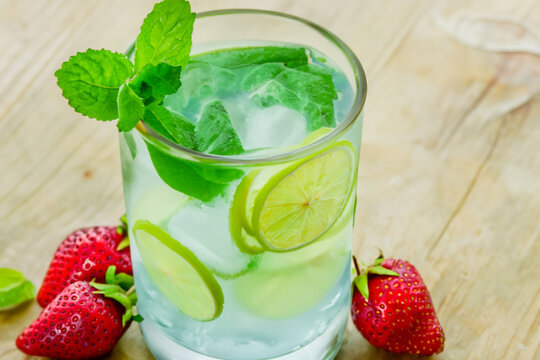 cold drink. in a transparent glass with water and ice there are slices of green lime and strawberries next to them