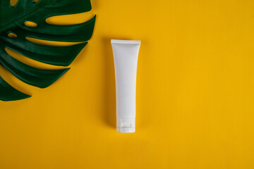 Cosmetic product in tube, bottle, lotion or serum on yellow background and tropical monstera leaves. 