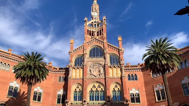 Entrance to Sant Pau Hospital, a masterpiece of Modernism architecture in Barcelona. Pan up to spire tower flanked by palm trees.