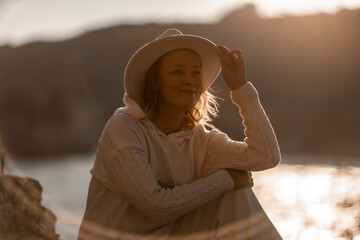 Happy blonde woman in a white suit and hat posing at the camera against the backdrop of the sea