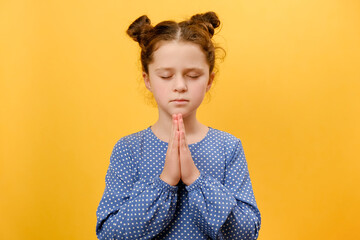 Portrait of pretty peaceful little girl with close eyes praying to God, making prayer gesture,...