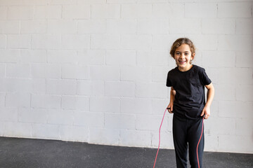 Horizontal photo elementary girl, smilingly jumping with rope in a gym. Copy space. Concept sport.