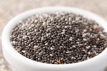 chia seeds. There is a white small plate with a lot of chia seeds on a light table, a health concept