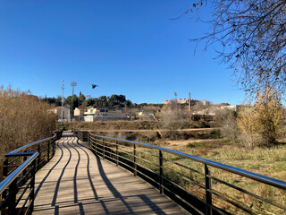 En las afueras de la ciudad de Sabadell. Puente de madera que cruza el río Ripoll. Día soleado. Vista al fondo de la Torre del Agua