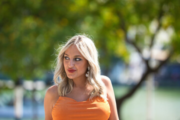Beautiful young woman posing against cityscape in bright orange dress. Female tourist in bright dress enjoys city views on sunny days. Concept of lifestyle, fashion, travel.