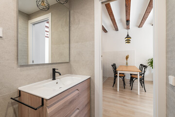 View from the bathroom with a sink and a mirror to the kitchen living area with a table and chairs waiting for the tenants. Concept of real estate and the work of realtors with new apartments