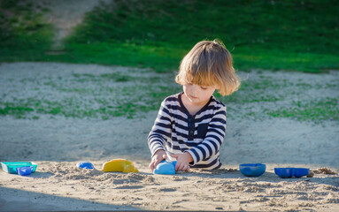 Cute little child boy having fun playing with sand and colorful toys in the park, beautiful summer sunny day in children playground. Selective focus