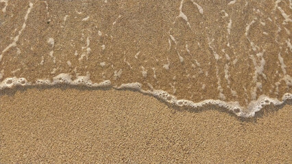 Golden sand with small waves on the beach. Top view with texture, great for holiday background