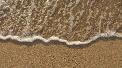 Golden sand with small waves on the beach. Top view with texture, great for holiday background