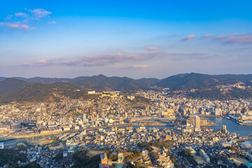 Fototapeta na wymiar Nagasaki cityscape panorama view from Mt Inasa observation platform deck in sunny day sunset time with blue sky background, famous beauty scenic spot in the world. Nagasaki Prefecture, Japan