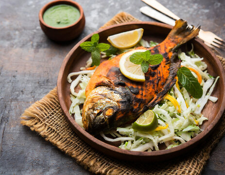 Tandoori Pomfret fish cooked in a clay oven and garnished with lemon , mint, cabbage and carrot salad