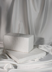 two stands made of white stone lie on a white satin draped background