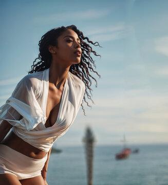 Black woman in a white dress with flowing hair looks into the seascape