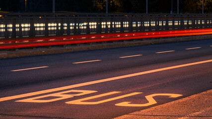 The word "BUS" written on the road for public transportation bus lane at night on bridge in urban environment