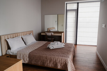 Hotel room interior. Double bed with towels, mirror, furniture, window.