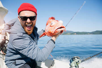 Happy Male fisherman holding red perch snapper big fish, Kamchatka Peninsula Russia. Deep sea sport...