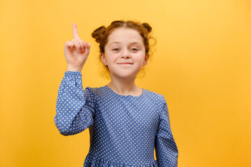 Portrait of inspired preteen girl child with open mouth pointing finger up in inspiration, having solution for problem, posing isolated over plain yellow color background wall in studio. Idea concept
