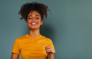 Beautiful happy dark skinned african american ethnicity woman in yellow tshirt raising hand in greeting while looking in camera with pleasant smile