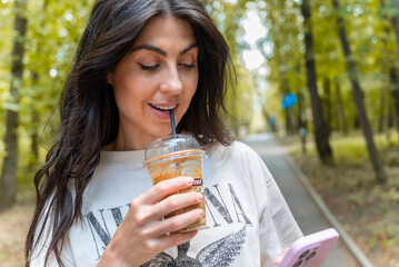 Woman walking in the summer park ,drinking coffee ,looking  her phone