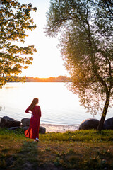 woman in red dress enjoying a peaceful sunset by the lakeside, the golden sunlight casting a warm glow on the serene waters