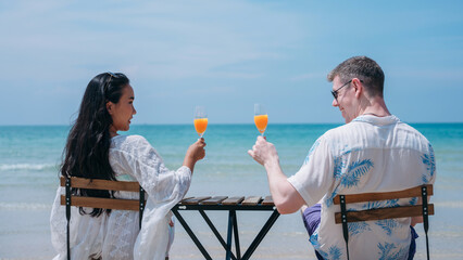 Obraz premium Happy and loving young couple drink orange juice at tropical beach. Couple Enjoying Fun and Romance by the Ocean.