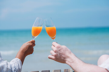 Happy and loving young couple drink orange juice at tropical beach. Couple Enjoying Fun and Romance...