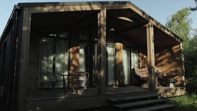 Cozy terrace in the wooden tiny house. Terrace in a small country house in the forest at summer. Table and brown sofa, shadows from trees on the wooden wall, slow motion.