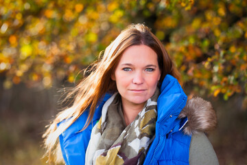 Young brunette woman head portraits with long hair in front of autumn tree.