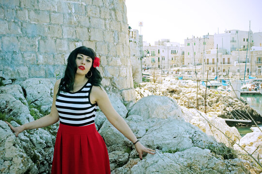 Harbor pin-up: Red skirt, stripes, retro glasses. Red heels, secrets beneath: garter belt, nude sheer stockings. Reimagined vintage elegance. 