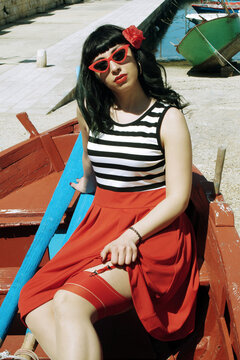 Harbor pin-up: Red skirt, stripes, retro glasses. Red heels, secrets beneath: garter belt, nude sheer stockings. Reimagined vintage elegance. 