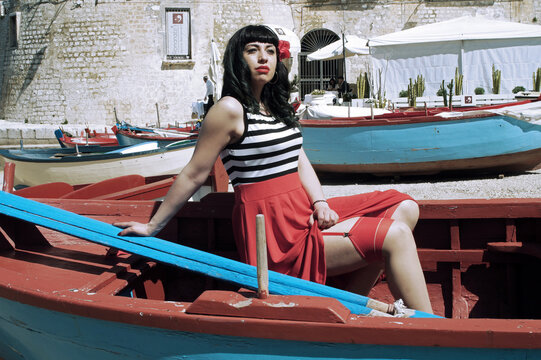 Harbor pin-up: Red skirt, stripes, retro glasses. Red heels, secrets beneath: garter belt, nude sheer stockings. Reimagined vintage elegance. 