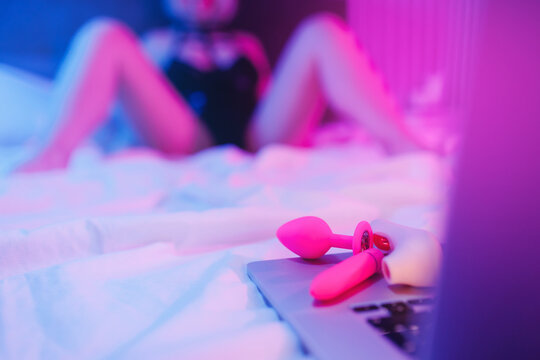 Beautiful woman lies in bed holding clitoral vibrator and watching porn on laptop, neon color. Women has Internet sex chat online