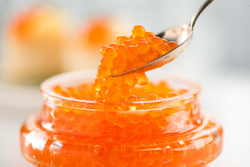 Red Caviar in a spoon, fish roe in a glass jar. Close-up of salmon fish roe caviar on served table. Delicatessen. Texture of fresh trout caviar. Backdrop. Seafood 
